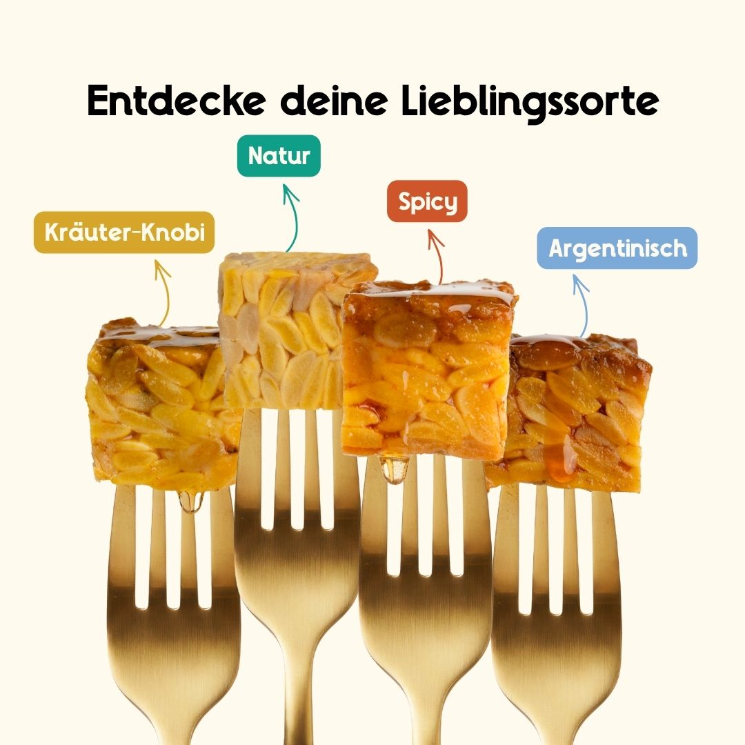 Nahaufnahme von vier verschiedenen Tempeh-Sorten auf goldenen Gabeln aufgespießt, die die unterschiedlichen Texturen und Marinaden zeigen.