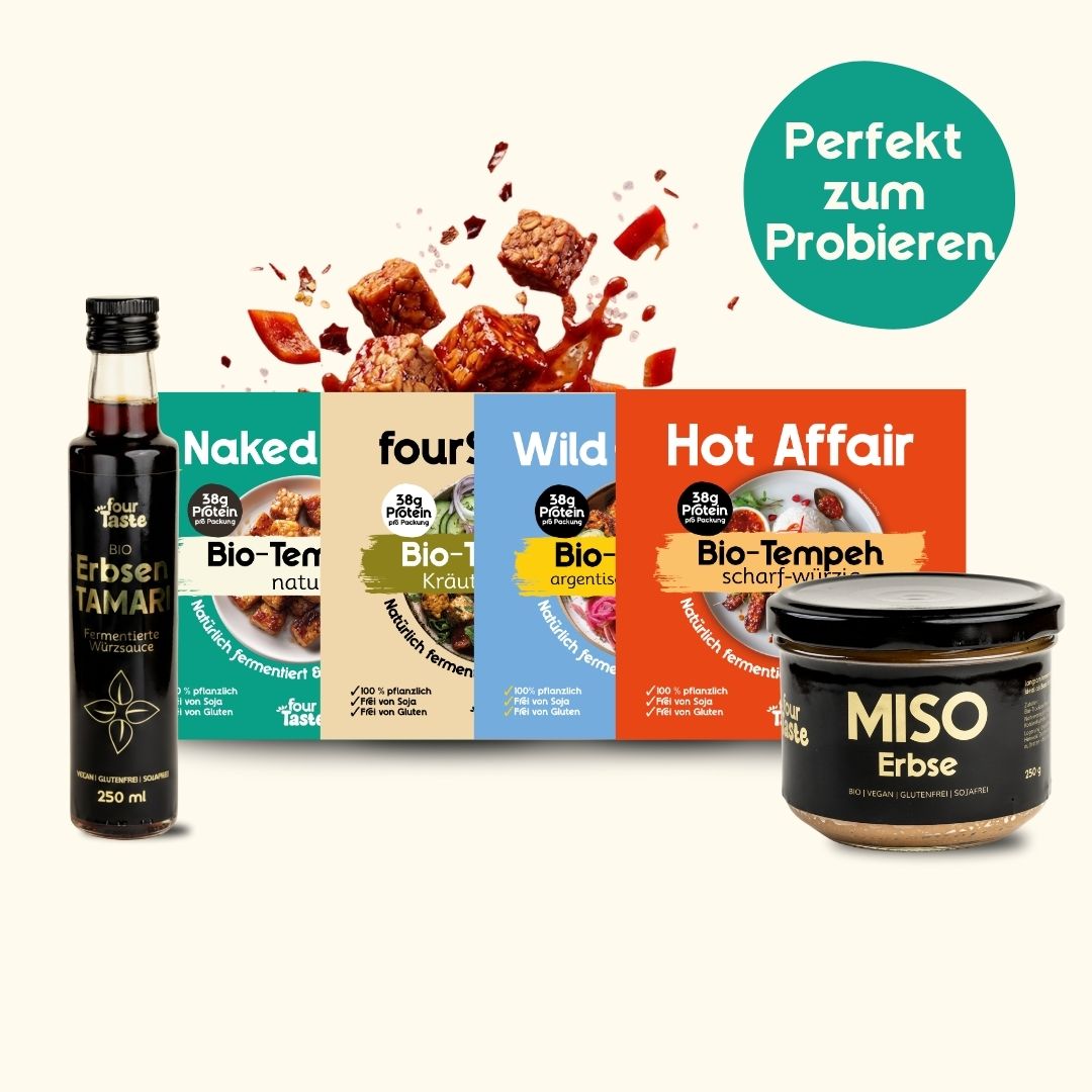 Produkt-Set bestehend aus 8 Packungen Bio-Tempeh in verschiedenen Sorten, einer Flasche Tamari-Sauce und einem Glas Miso-Paste, dekoriert mit frischen Zutaten wie Knoblauch und Zwiebeln.