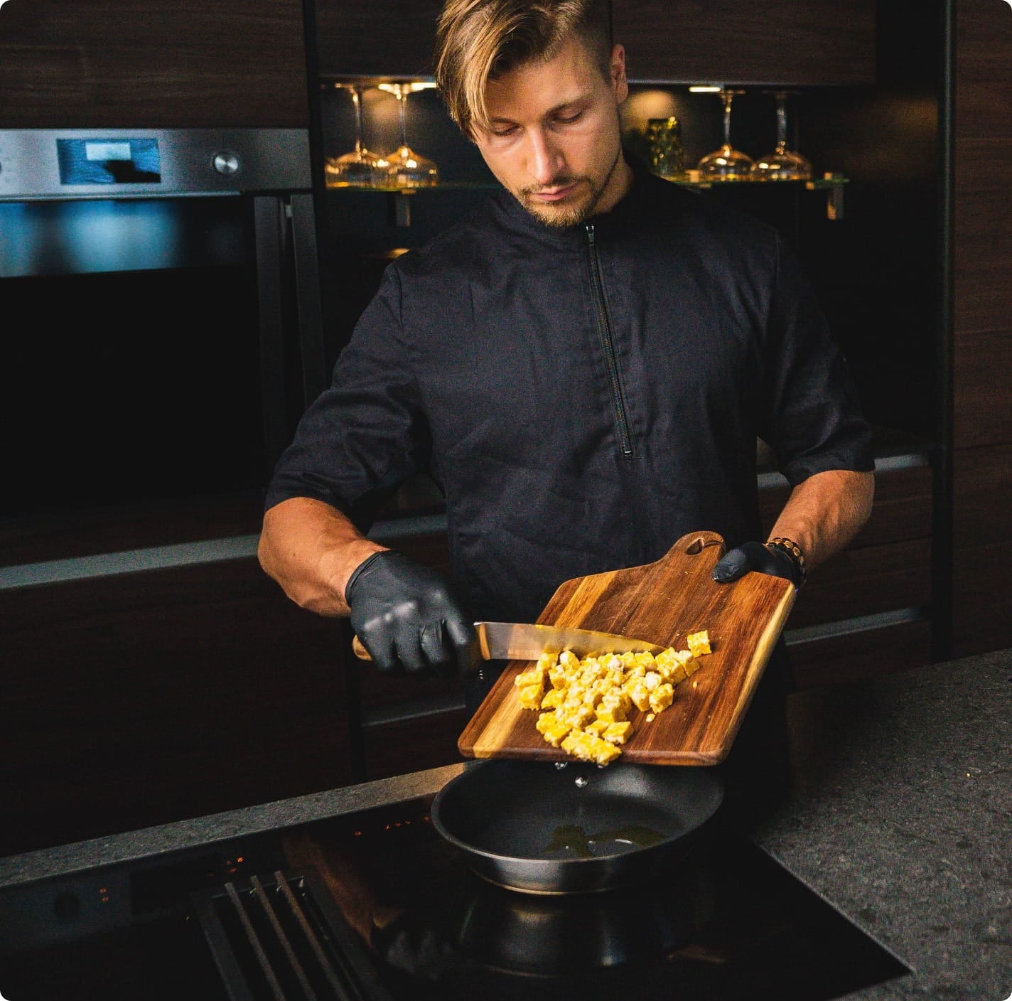 Koch schiebt gewürfelten Tempeh von Holzbrett in eine Pfanne